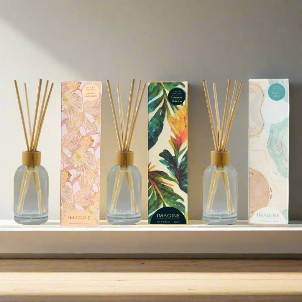Set of three diffuser bottles with wooden sticks and decorative boxes on a white background