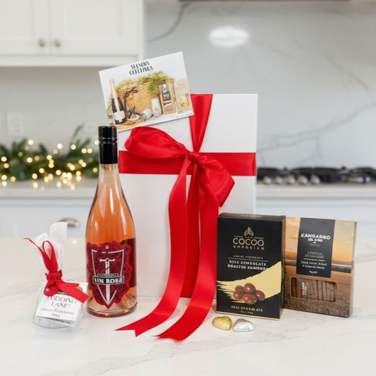 Gift basket with a bottle of wine, chocolates, and a card on a kitchen counter.
