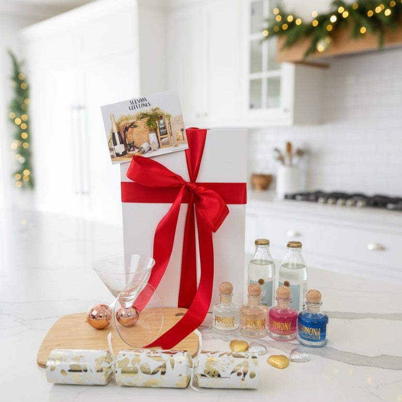 Gift box with red ribbon on a kitchen counter with mini bottles and glasses.